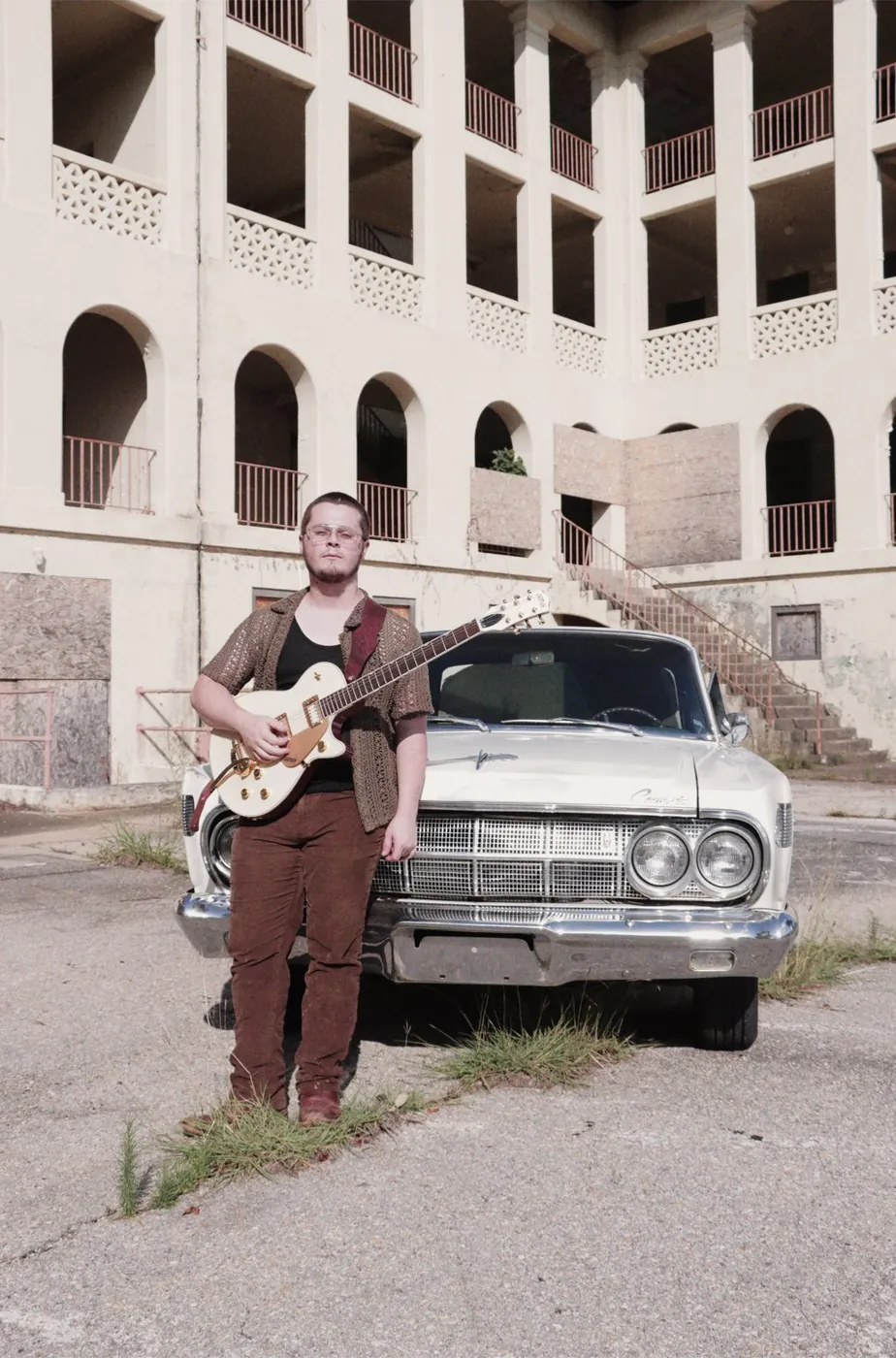 Tyler Nichols with a guitar in front of a vintage car