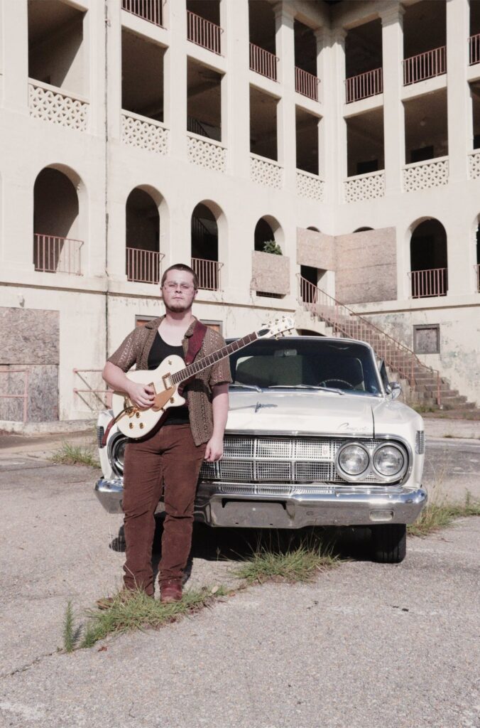 Tyler Nichols standing with a white Gretsch guitar in front of a vintage car