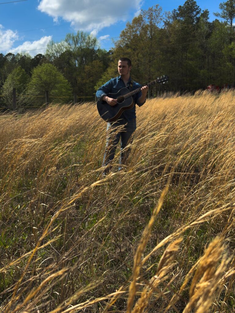 Tyler Nichols playing acoustic guitar in a golden field
